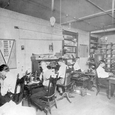 Five young men sitting at desks in a newsroom.