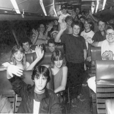A group of children on a bus waving to the camera.