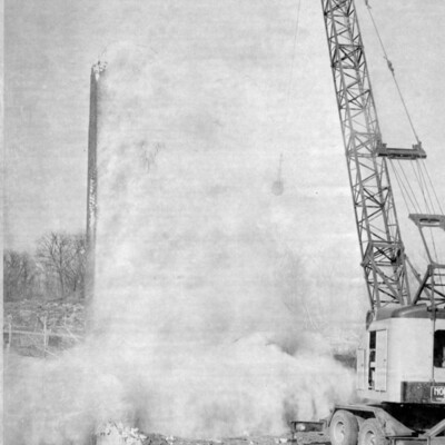 Tall crane in front of cloud of smoke from the demolition of a tower.