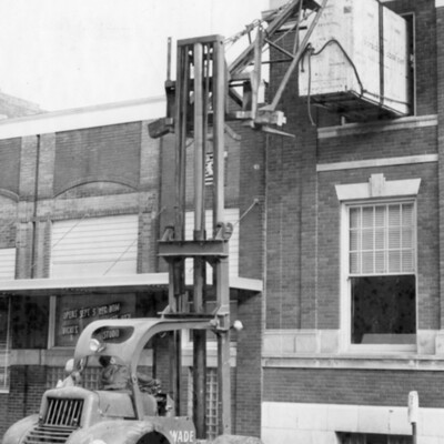 A large piece of equipment atop a hoist in front of a building.